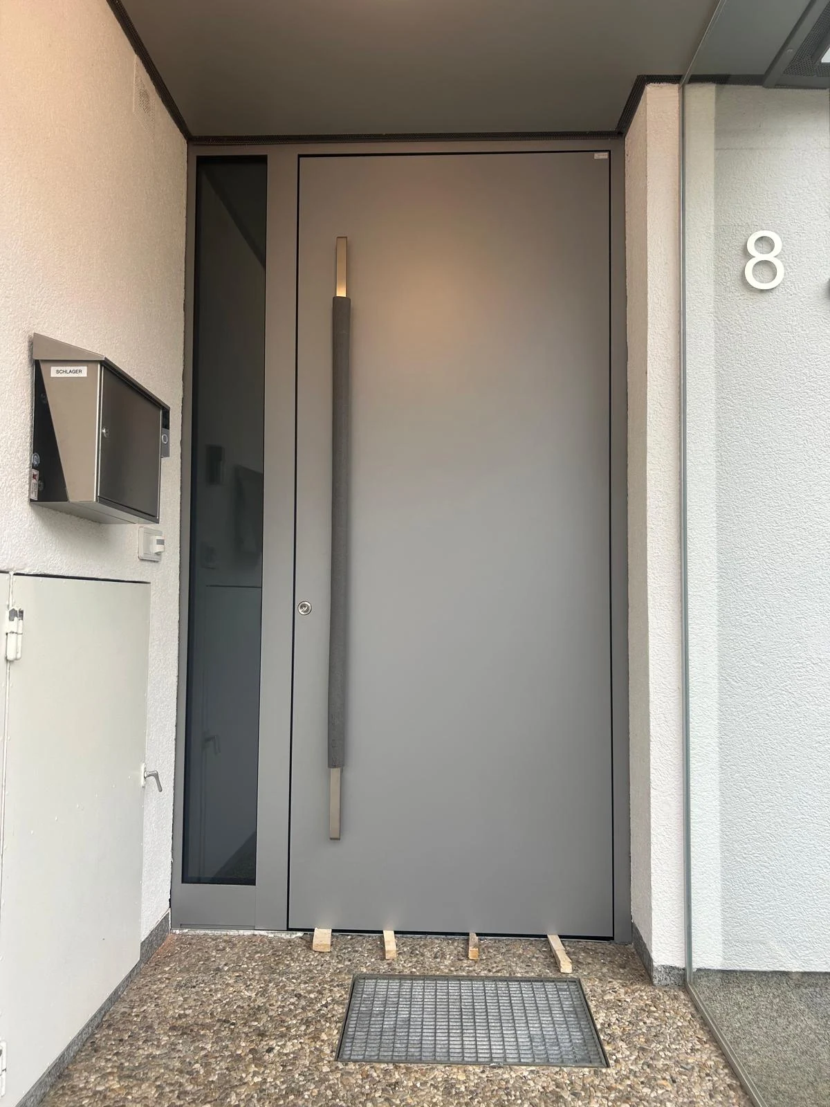 Graue Haustür mit langem Griff und seitlichem Glaselement